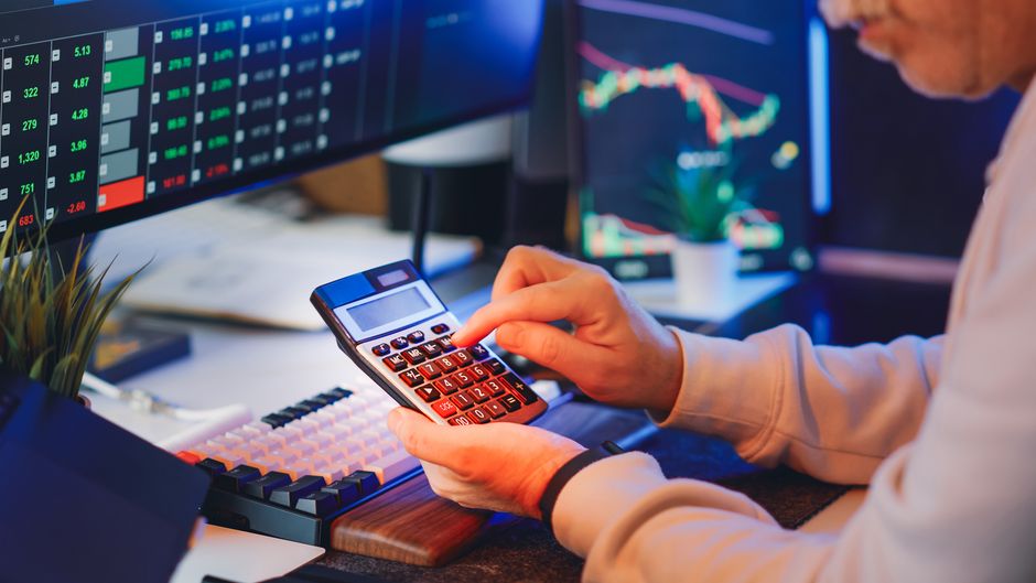 Person using a calculator in a digital office for stock market analysis.